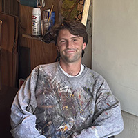 Man in paint-splattered shirt sitting in a chair
