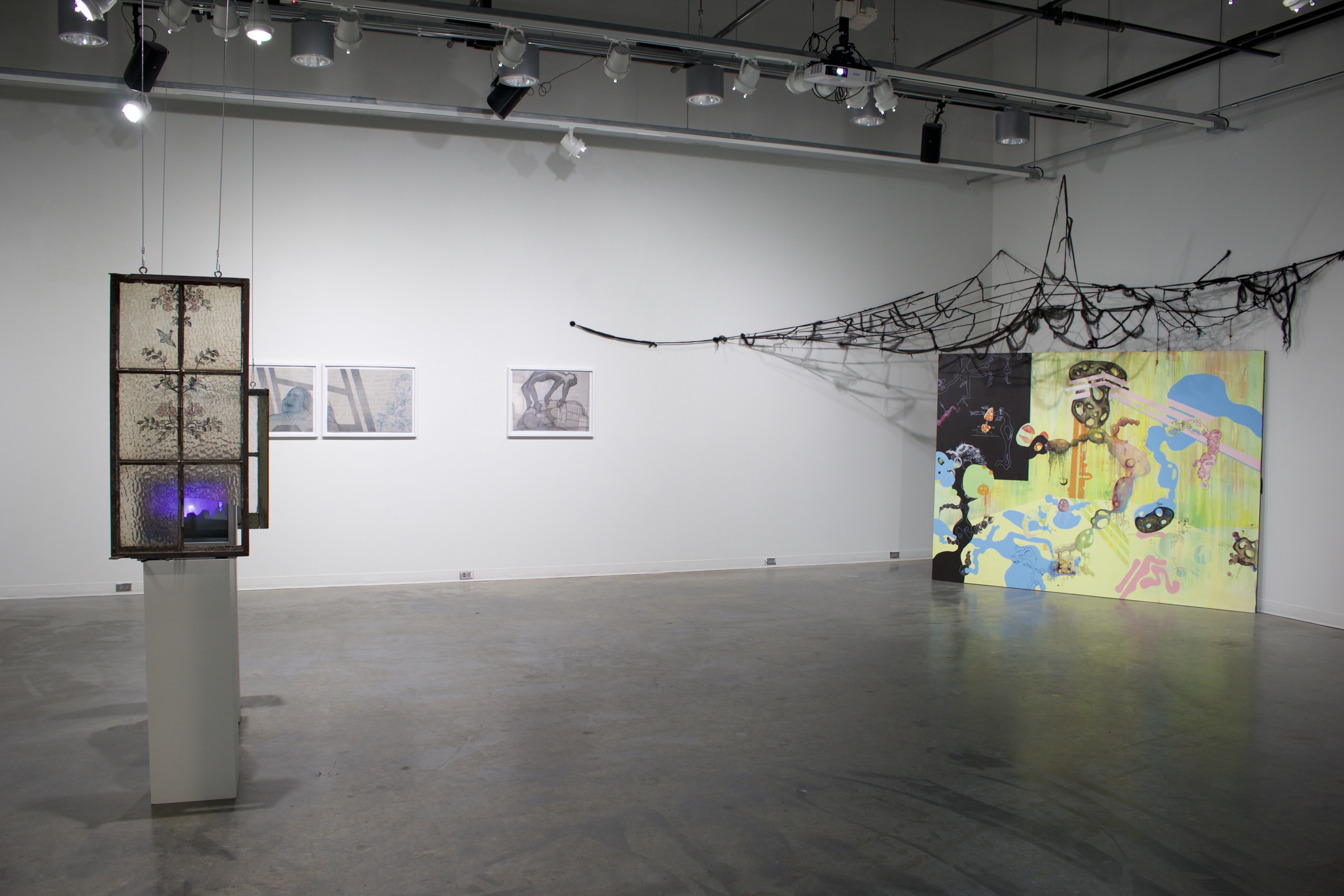 Art gallery with multiple artworks including a hanging window frame, three framed prints, and a large yellow painting with a net made of hair hanging overhead.