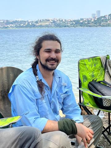 bearded man smiling while sitting near a body of water