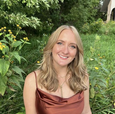 Woman with long hair sitting amidst vegetation and looking at the viewer