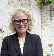 Woman near a brick wall wearing glasses and a sportcoat